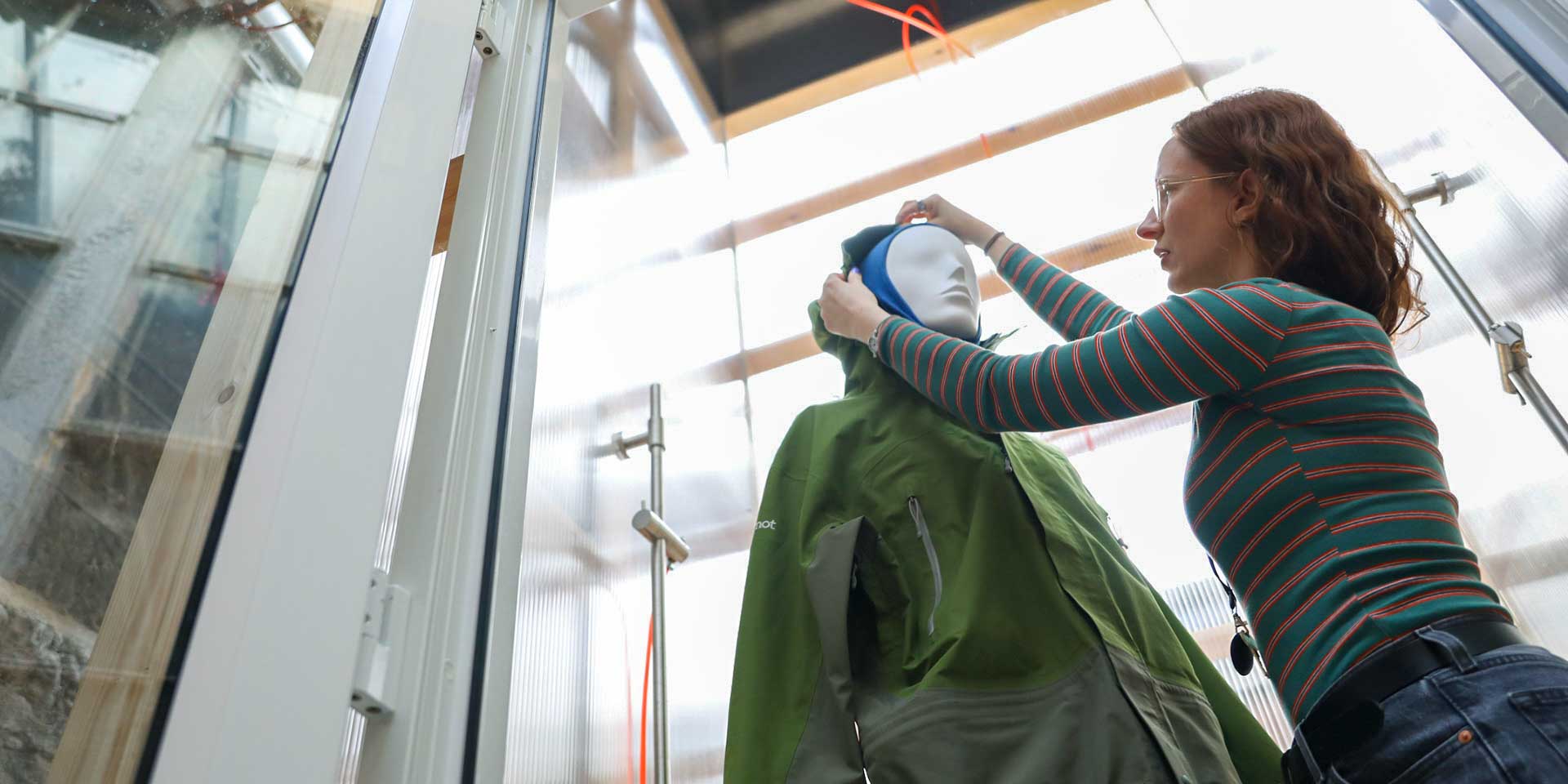 A researcher fitting a waterproof jacket onto a mannequin inside an environmental weather testing chamber.